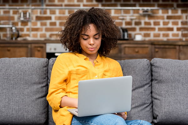 Woman On Sofa Wearing Yellow Looking At Laptop