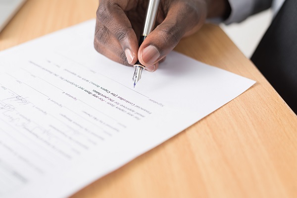 Hand Signing Form On Wooden Desk