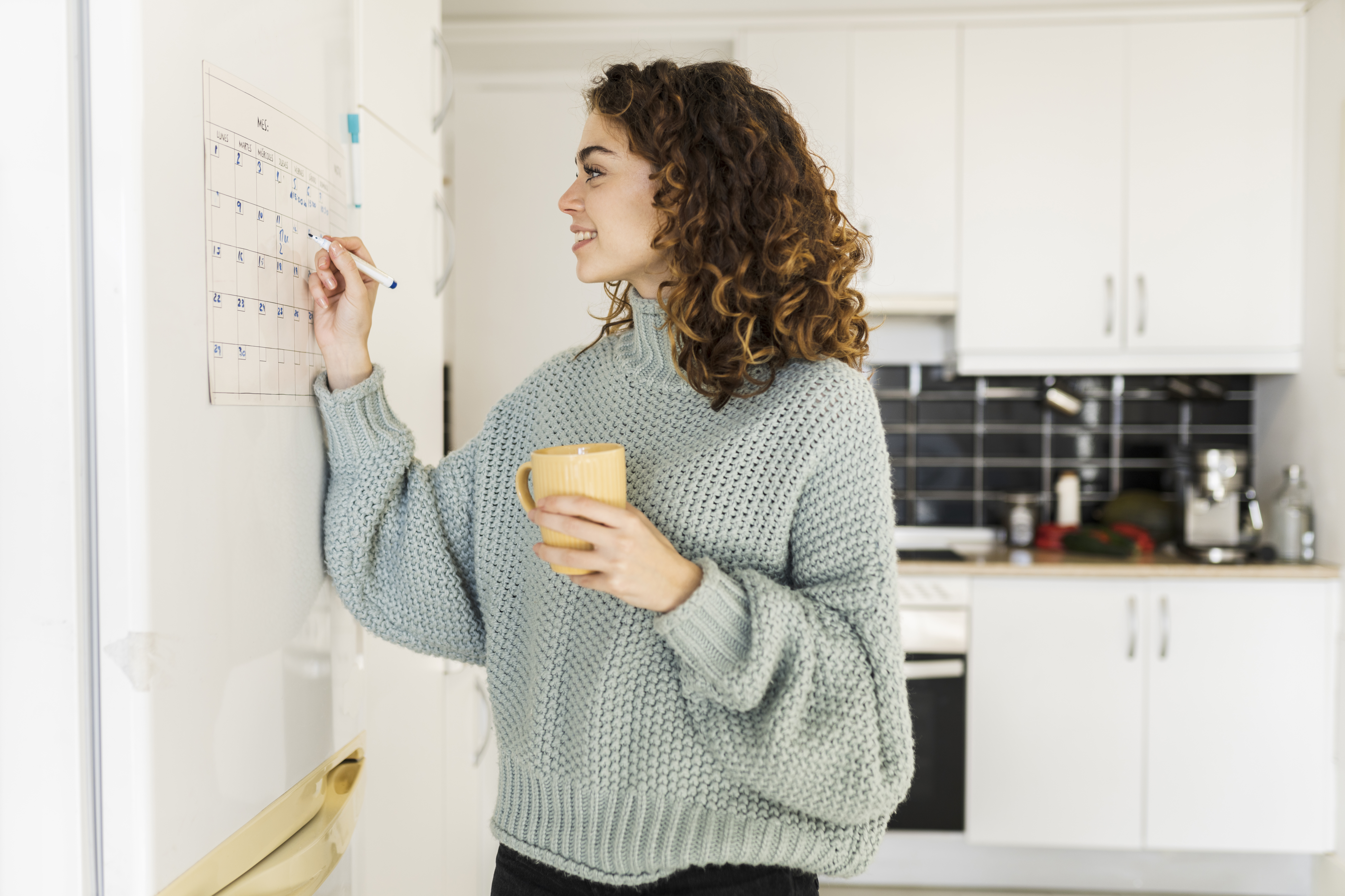 Woman Looking At Calendar In Kitchen Holding Mug