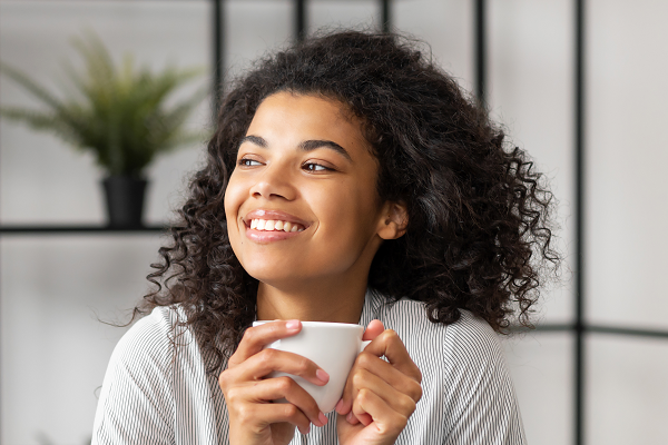 Woman Looking Out Of Window Smiling Holding Tea