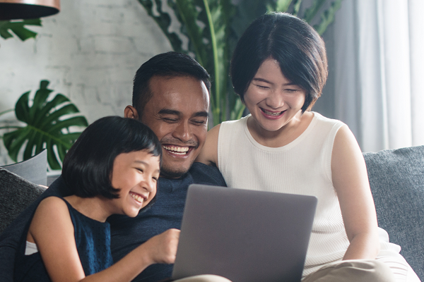 Young Family Smiling Looking At Laptop On Sofa