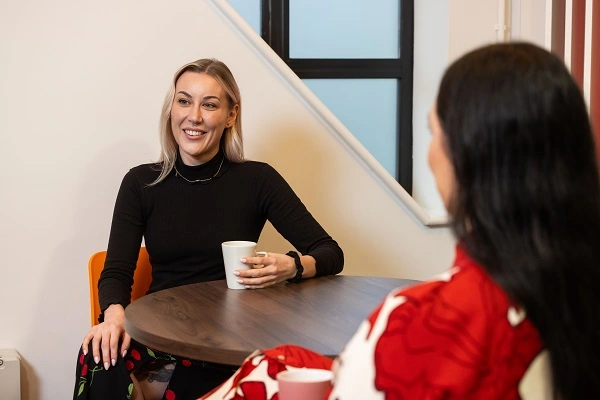 Two Women Sitting At Round Table Drinking Coffee
