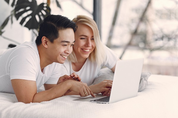 Couple Smiling On Bed Looking At Laptop